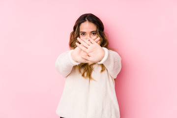 Young curvy woman posing in a pink background isolated doing a denial gesture