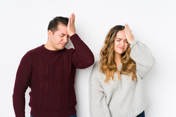 Young couple posing in a white background forgetting something, slapping forehead with palm and...