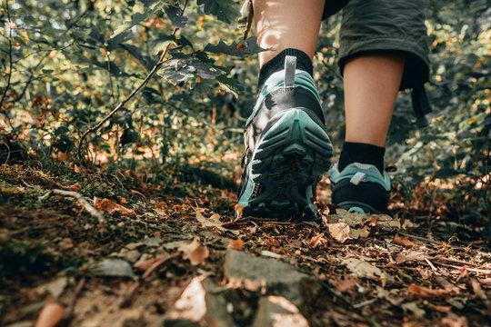 Muddy boots of hiker on forest trail. Traveler feet are stepping on the ground with fallen leaves. Close up of the sole of dirty shoes. Adventure and hiking concept outdoor. Hipster lifestyle