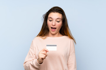 Fototapeta premium Young brunette girl over isolated blue background holding a credit card