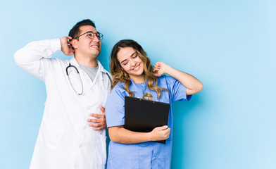 Young doctor couple posing in a blue background isolated stretching arms, relaxed position.