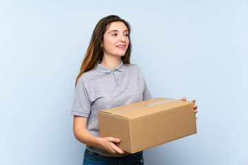 Young brunette girl over isolated blue background holding a box to move it to another site