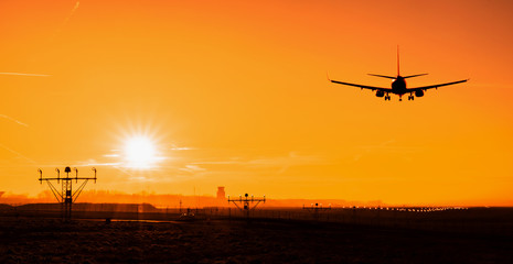 Back view silhouette of airplane landing at the airport at sunny orange and purple sunset. Runway...