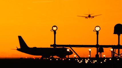 Silhouette of airplanes at the airport at sunny orange and purple sunset. Plane taxiing on the...
