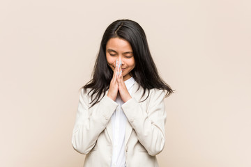 Young business chinese woman holding hands in pray near mouth, feels confident.