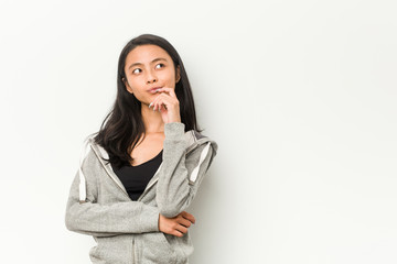 Young fitness chinese woman looking sideways with doubtful and skeptical expression.