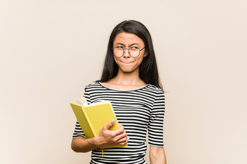 Young asian woman student holding a book confused, feels doubtful and unsure.