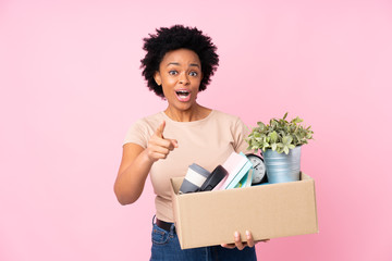 African american woman making a move while picking up a box full of things surprised and pointing...