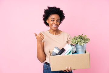 African american woman making a move while picking up a box full of things pointing to the side to...