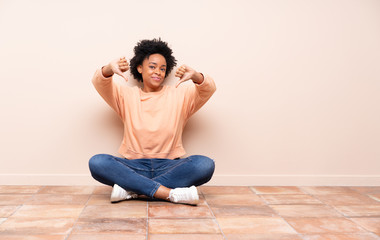 African american woman sitting on the floor showing thumb down