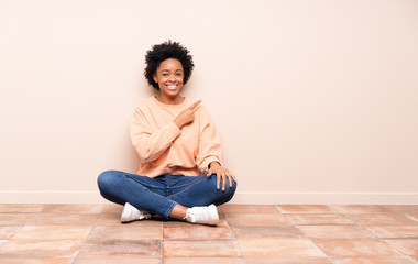 African american woman sitting on the floor pointing to the side to present a product