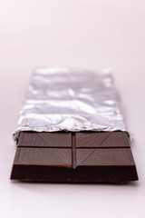Fototapeta na wymiar Dark chocolate with whole hazelnuts in aluminum foil isolated on white background