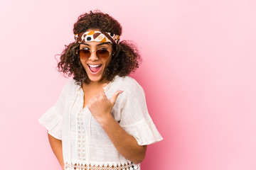Young african american hipster woman isolated on pink background points with thumb finger away, laughing and carefree.