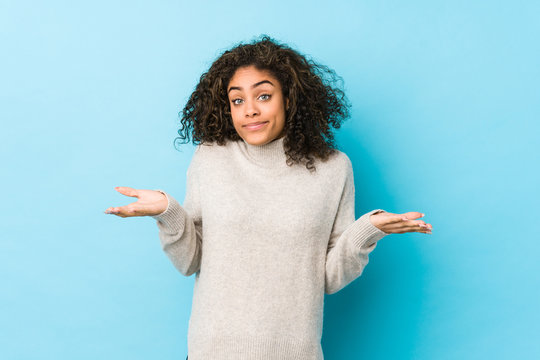 Young african american curly hair woman doubting and shrugging shoulders in questioning gesture.