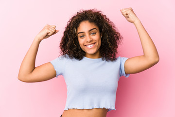 Young african american woman against a pink background showing strength gesture with arms, symbol...