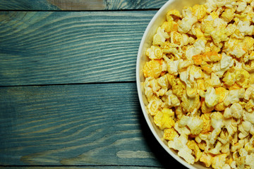 Yellow caramelized popcorn in white bowl over blue wooden background.  Fast food, junk food. Abstract colorful food background.