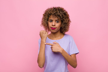 young african american woman looking impatient and angry, pointing at watch, asking for...