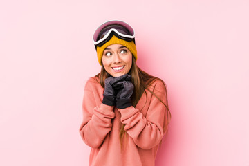 Young caucasian woman wearing a ski clothes isolated keeps hands under chin, is looking happily aside.