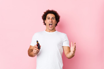 Young caucasian curly man holding a vape celebrating a victory or success