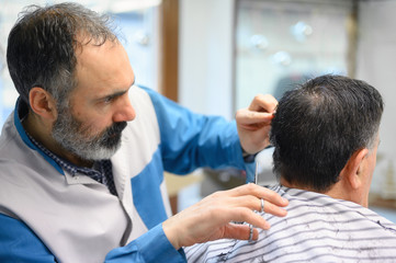 Fototapeta premium Barber trimming hair of old man at barber shop .