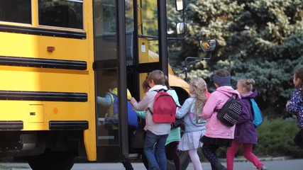 Cute schoolkids running in crowd to school bus standing with open doors near school. Happy elementary age children rushing home after lessons and pushing while getting on school bus waiting for them