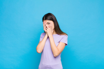 young pretty woman feeling scared or embarrassed, peeking or spying with eyes half-covered with...