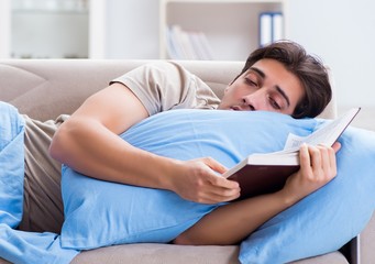 The young student man preparing for college exams in bed with bo