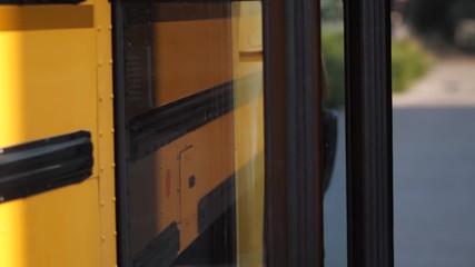 Joyful cute elementary age schoolkids in friendly crowd boarding school bus opening doors for them. Happy diverse schoolchildren running into open doors of yellow bus after day of study