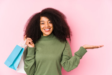 Young afro woman shopping isolated Young afro woman buying isolaYoung afro woman holding a roses isolated showing a copy space on a palm and holding another hand on waist.< mixto >