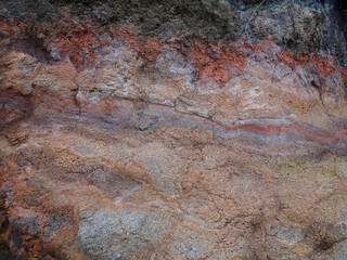 Mottled color of purples and grays and reds show in this picture of a dirt cliff alongside a road in Maui.