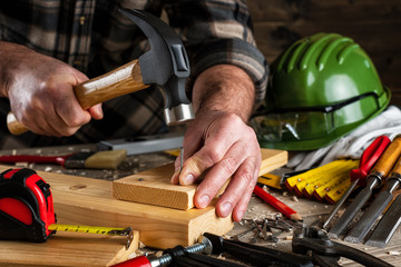 Close-up. Carpenter with hammer and nails fixes a wooden board. Construction industry, do it yourself. Wooden work table.