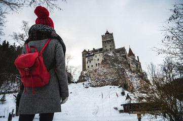 Beautiful young woman watching a medieval castle and dressed in winter clothes. Bran Castle, better known as Dracula's Castle