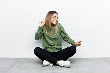 Fototapeta premium Young caucasian woman sitting on the floor dancing and having fun.