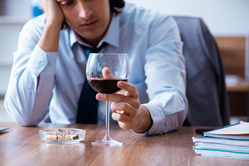 Male employee drinking alcohol and smoking cigarettes at workpla