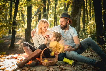 Basket with picnic meal and toys for the kid. Happy family of three lying in the grass in autumn. The concept of a happy family. Young smiling family doing a picnic on an autumns day.