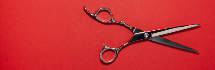 Banner flat lay of professional hair cutting shears on the right side on red background....