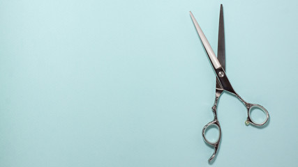 Flat lay of professional hair cutting shears on the right side on blue background. Hairdresser salon equipment concept with copy space