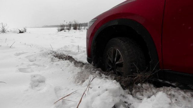 The car got stuck in snow and dug a hole with wheel, in the snowfall. Red machine on snow-covered road. Red machine on snow-covered road. Automobile in winter in slow motion.