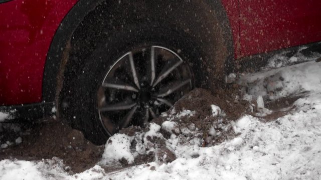 The wheel of car slides on the snow and the ground, can not leave. Red car on snow-covered road. Wheel slides on the snow, stuck in a snowdrift, closeup view. Wheel rotates in the snow in slow motion.