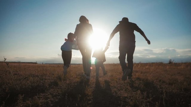 Happy young family together with children at sunset. People silhouettes on summer sunset meadow. Concept of friendly family.