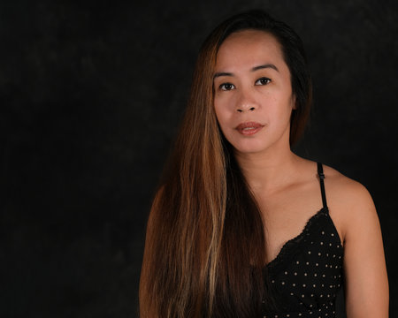 Beautiful young brunette Filipina woman posing in studio on dark background
