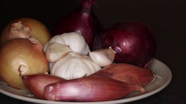 Close-up pan of different onions and garlic on a plate with dark background