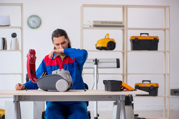 Young male contractor repairing vacuum cleaner at workshop