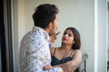 An young and attractive Indian Bengali brunette couple wearing western wear smoking cigarette together in a funny mood in the balcony. Indian lifestyle.