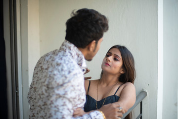 An young and attractive Indian Bengali brunette couple wearing western wear smoking cigarette together in a funny mood in the balcony. Indian lifestyle.