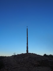 Fototapeta premium Beautiful blue sky with Cruz de Ferro (Cross of Iron) in the early morning on the road to Santiago de Compostela, Camino de Santiago, Way of St. James, Foncebadon to Ponferrada, French way, Spain