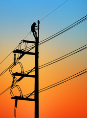 Silhouette Electrical engineers working on electricity pylon high tension power line repairs and maintenance  on blurry sunset background