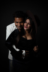 Close up portrait of an young and attractive Indian brunette Bengali couple with western dresses and cowboy hat in black studio copy space background. Indian fashion portrait and lifestyle