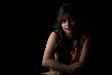 Obraz na płótnie Canvas Close up fashion portrait of an young and attractive Indian Bengali brunette girl with colorful western dress in front of a black studio copy space background. Indian fashion portrait and lifestyle.