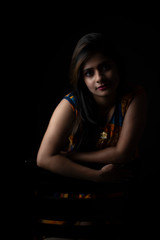 Close up fashion portrait of an young and attractive Indian Bengali brunette girl with colorful western dress in front of a black studio copy space background. Indian fashion portrait and lifestyle.